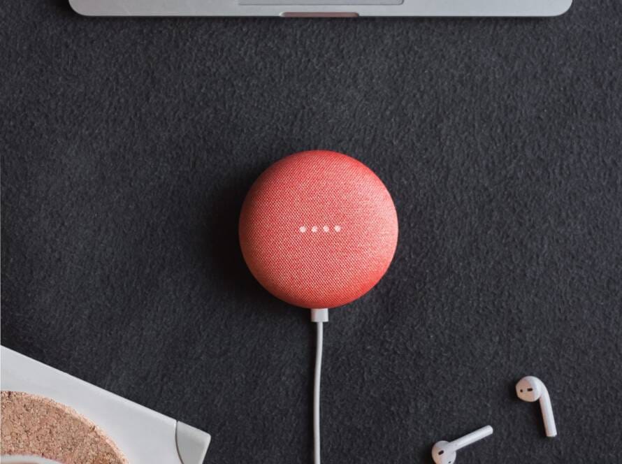 flat lay photography of coral Google Home Mini on black surface beside Apple AirPods